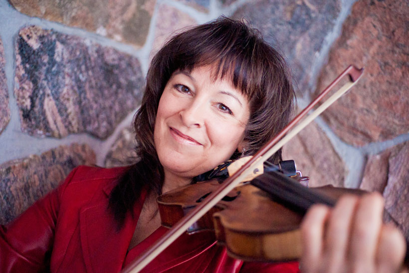 A photo of Cindy Thompson smiling and playing her fiddle.